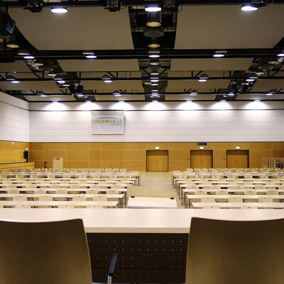 Das Bild zeigt mit Blick von der Bühne den gesamten Saal der Lindenhalle, in dem eine parlamentarische Bestuhlung aus Stühlen und Tischen aufgebaut ist.