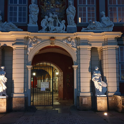 Das Portal des Schlosses Wolfenbüttel bei Nacht, die beiden Figuren rechts und links neben dem Torbogen werden durch Bodenstrahler angestrahlt.