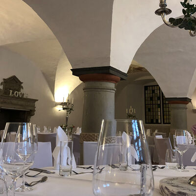 Im Renaissancesaal auf Schloss Wolfenbüttel stehen festlich eingedeckte Tische mit weißen Tischdecken und Servietten und hohen silbernen Leuchtern sowie Blumenschmuck. Im Hintergrund ist ein Kamin zu erkennen.