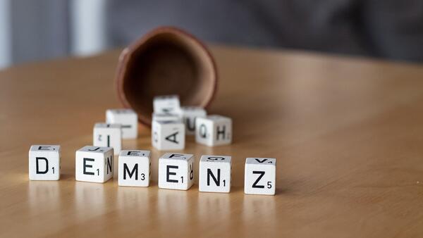 Auf einer Tischplatte liegen vor einem Würfelbecher mehrere Buchstabenwürfel. Einige davon bilden das Wort "Demenz".